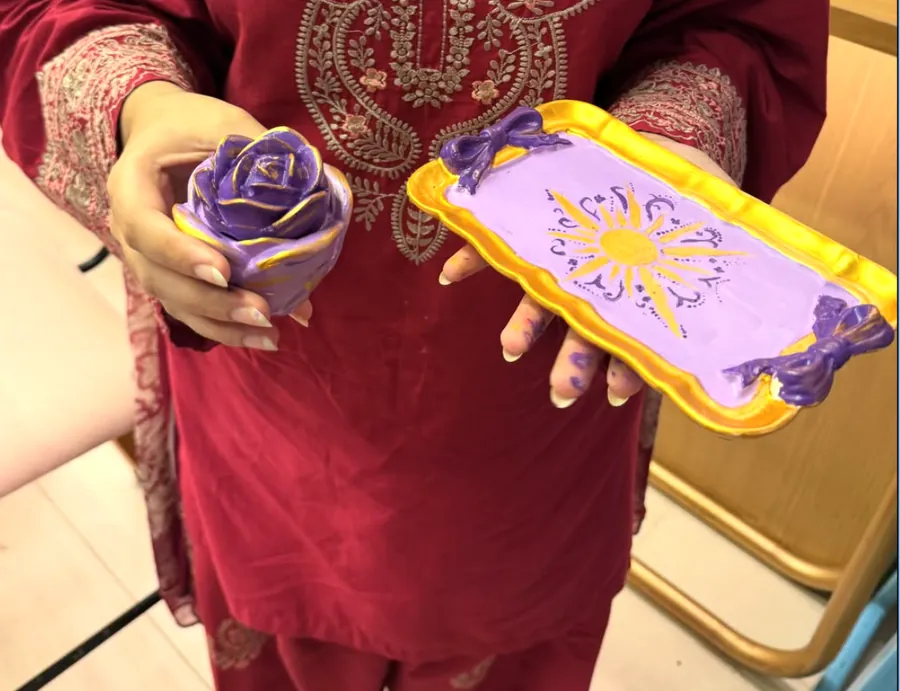 A guest holding a purple and gold painted tray and matching rose-shaped piece